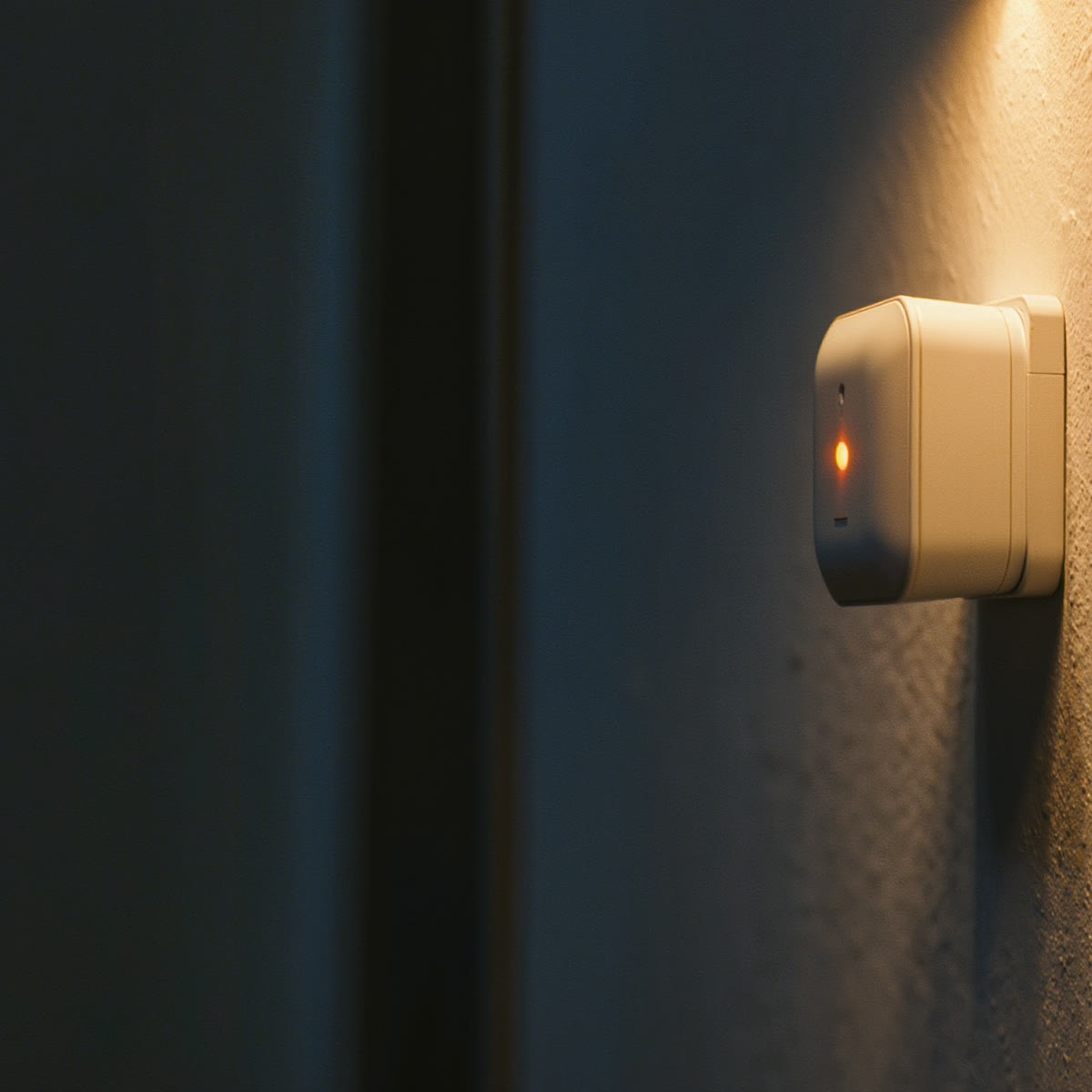 A small warm-white sensor the size of a credit card plugged into a wall outlet, glowing soft amber.